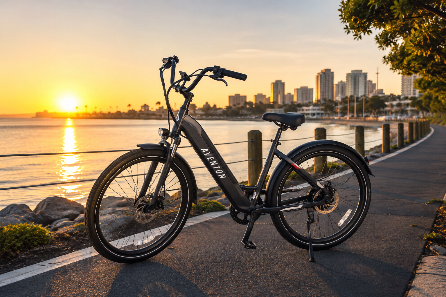 Aventon Pace 4 electric bike parked beside a waterfront trail during sunrise with a scenic city skyline in the background.