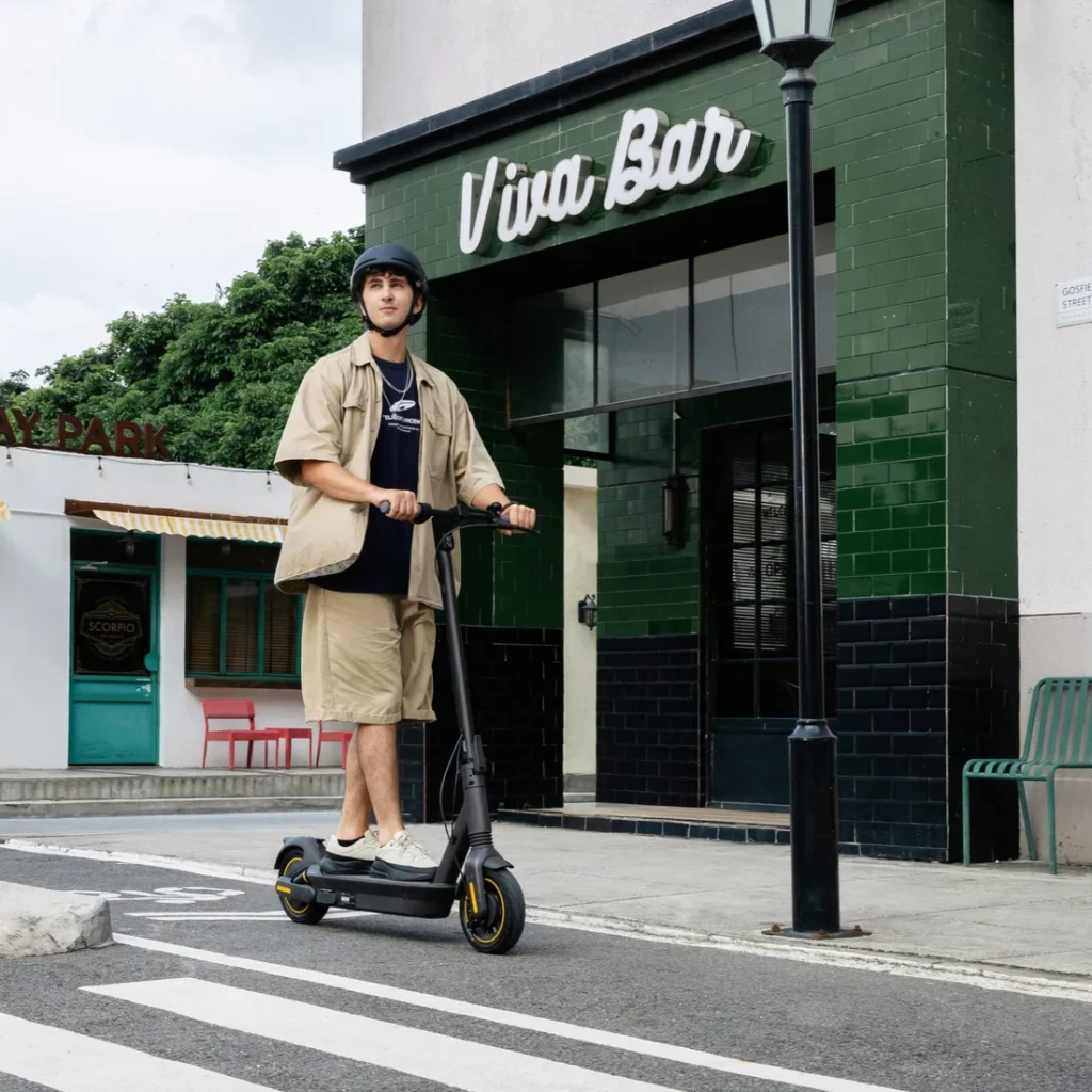A young man wearing a helmet riding a Segway electric scooter down a city street past a green storefront labeled "Viva Bar".