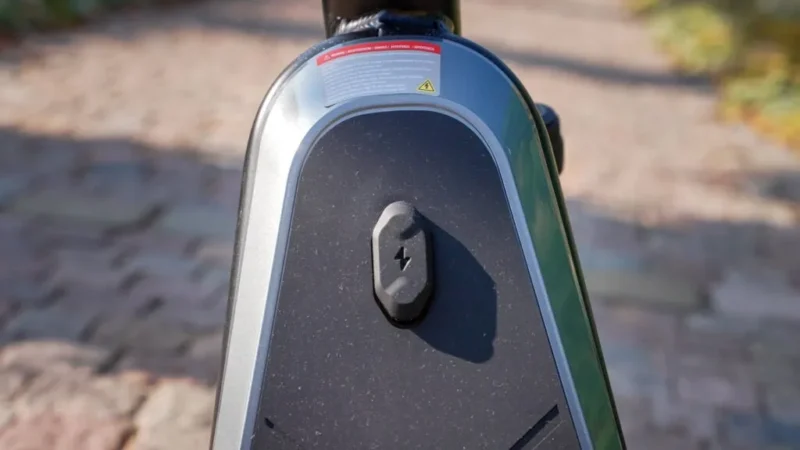 Close-up outdoor shot of the charging port covered by a rubber flap on the front stem enclosure of the NIU KQi300X.