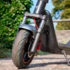 Close-up shot of the front wheel, hydraulic fork suspension, and red brake disc assembly of the NIU KQi300X on a stone path.