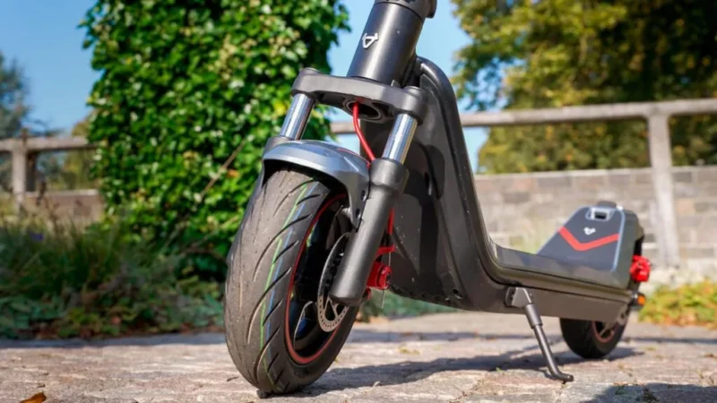 Close-up shot of the front wheel, hydraulic fork suspension, and red brake disc assembly of the NIU KQi300X on a stone path.