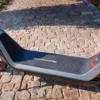 Close-up outdoor shot of the wide foot deck on the NIU KQi300X featuring the "MAKE LIFE ELECTRIC" branding text and kickstand down.