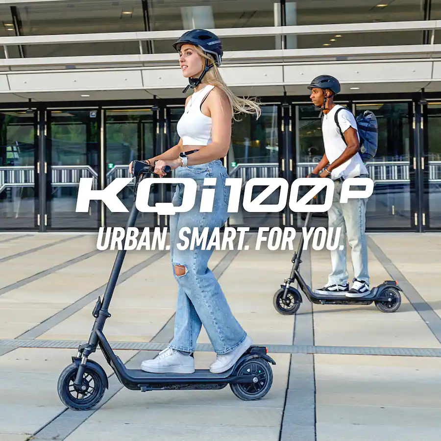 A young woman and man riding KQi100P electric scooters outside a modern urban building.