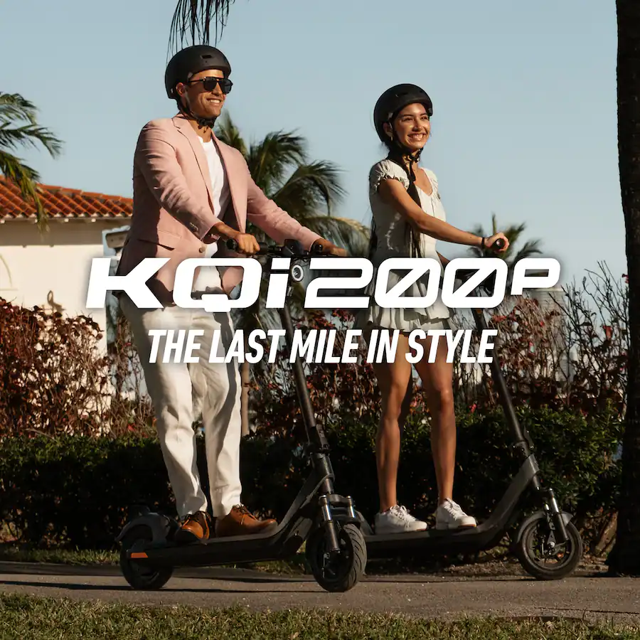 A man in a pink blazer and white pants and a woman in a light-colored dress, both wearing black helmets, ride their dark gray NIU KQi 200P electric scooters side-by-side on a paved path lined with tropical plants and a white house. White text overlay reads "KQi 200P" and "THE LAST MILE IN STYLE".