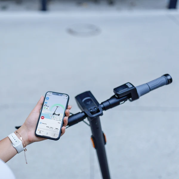 A person holding a smartphone displaying the NIU app interface next to the handlebars of an electric scooter.