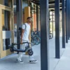 A man carrying a folded NIU KQi 100P electric scooter under his arm while walking outside an office building.