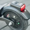 Close-up of the rear wheel hub, disc brake components, and red tail light assembly on an electric scooter.