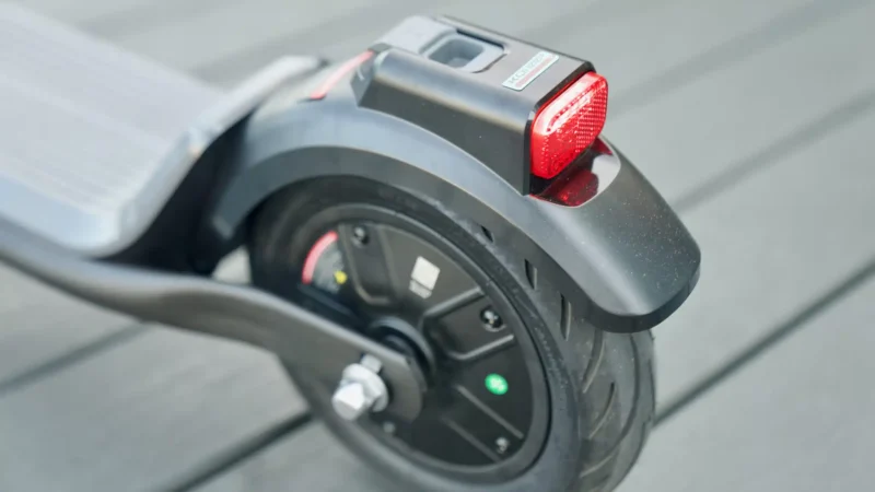 Close-up of the rear wheel hub, disc brake components, and red tail light assembly on an electric scooter.