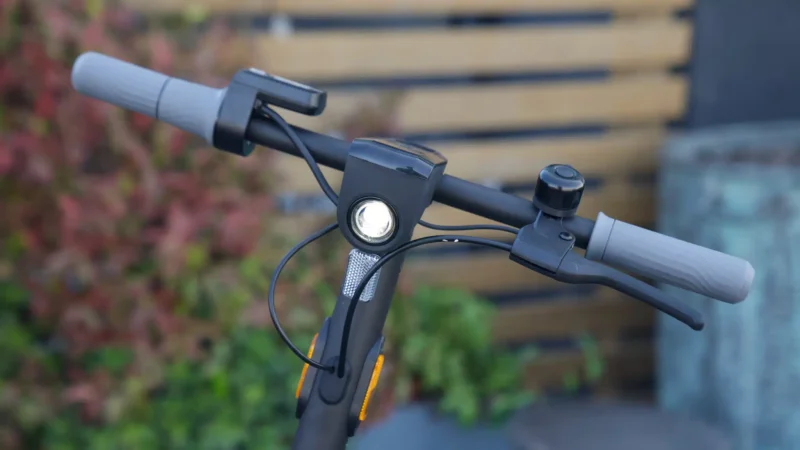 Front-facing view of electric scooter handlebars with an illuminated high-intensity LED headlight and side reflectors.