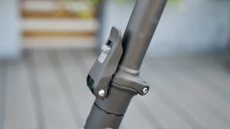 Close-up of the quick-release folding latch mechanism on the steering column of a dark gray electric scooter.