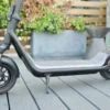 Full side profile of a dark gray electric scooter on a wooden deck, showing the dual tube front suspension and standing deck.