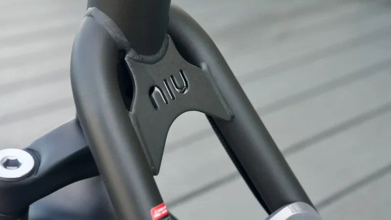 Close-up of the reinforced black metal steering fork junction featuring the embossed NIU brand logo