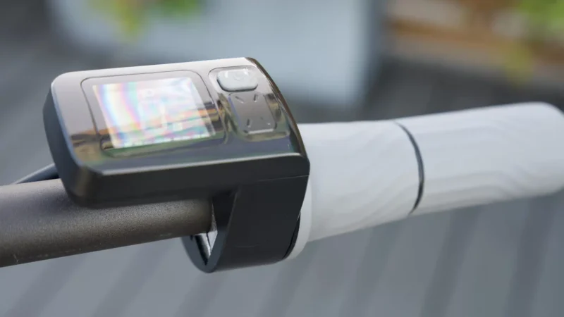 Close-up of the digital handlebar display screen and right rubber grip on an electric scooter.