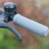 Close-up of a black hand brake lever, manual bell, and textured gray rubber handlebar grip.