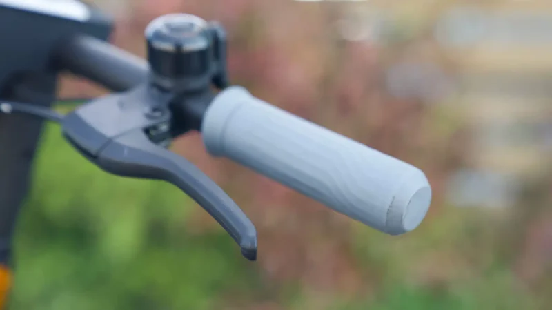 Close-up of a black hand brake lever, manual bell, and textured gray rubber handlebar grip.